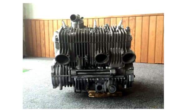 Bloc Moteur Moto 3 Cylindres avec Ailettes de Refroidissement Bloc moteur de moto à trois cylindres avec ailettes de refroidissement en aluminium sur un fond de mur en bois.