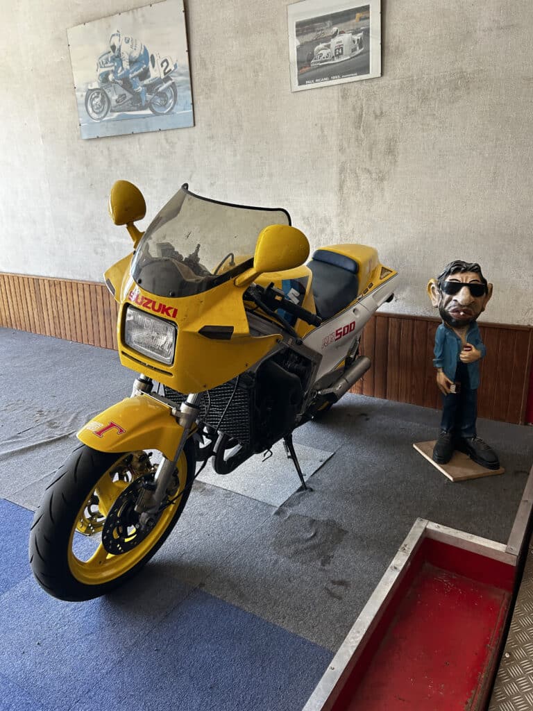 Moto Suzuki RG500 Jaune : Modèle de Collection Vintage Moto Suzuki RG500 jaune, figurine caricaturale et affiches de course en arrière-plan.